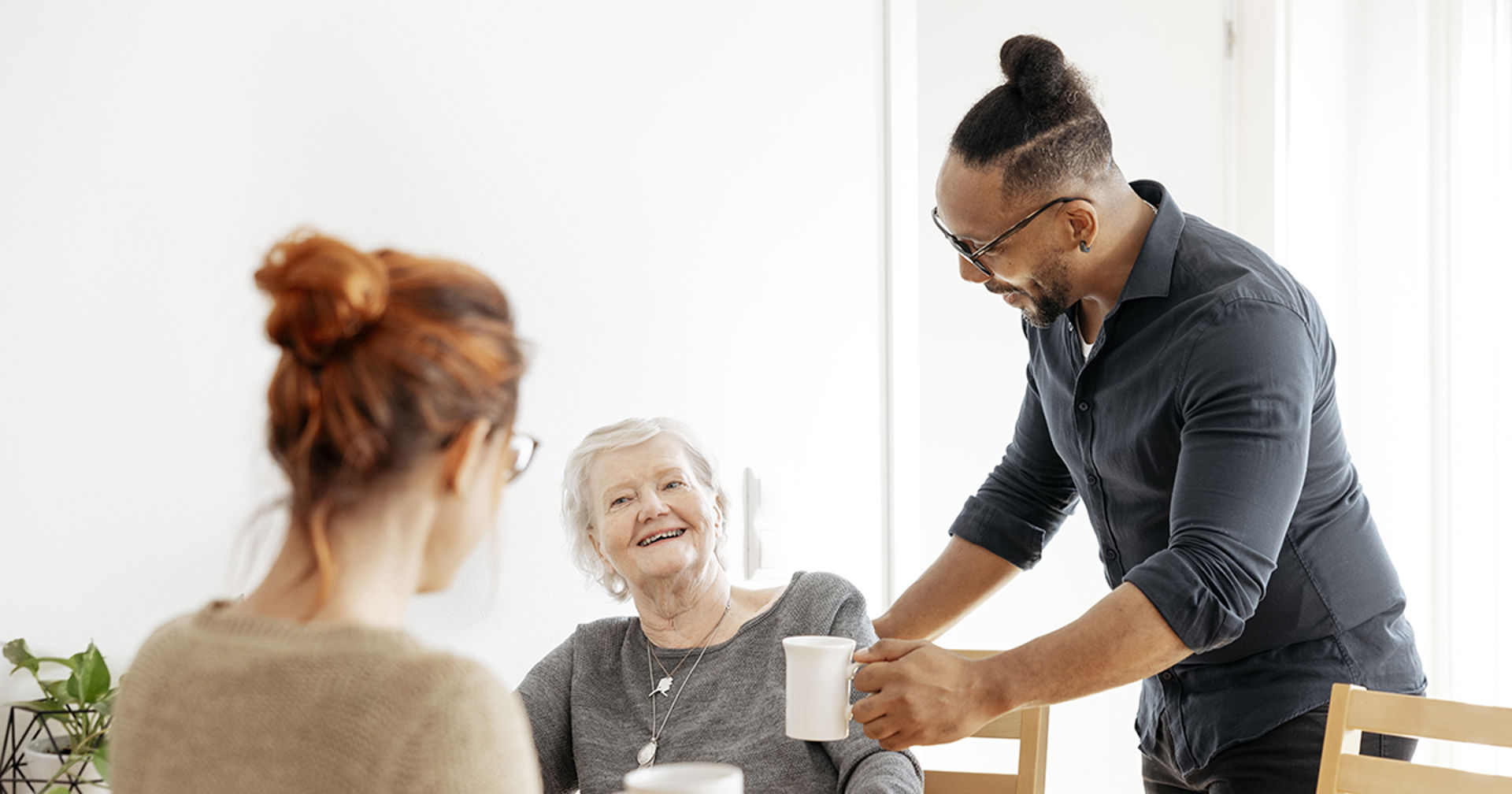 Två personer sitter. Den tredje räcker dem en liten kanna.