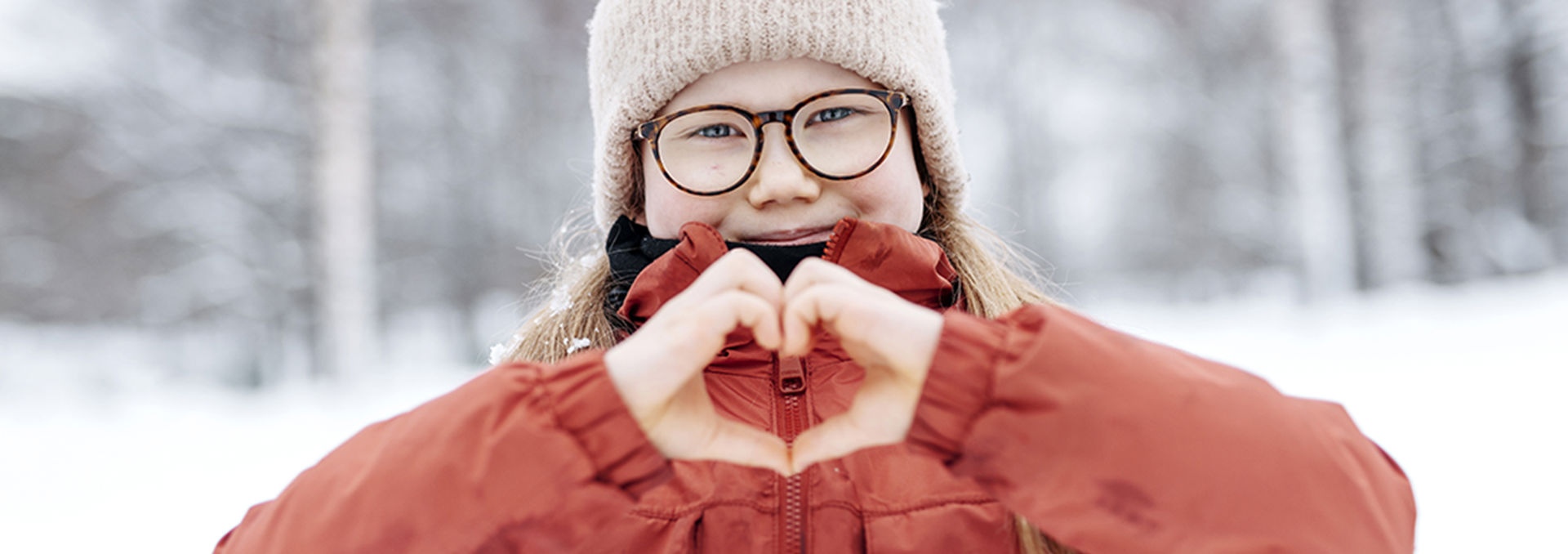 Barnet gör ett hjärta med sina händer och ler mot kameran.