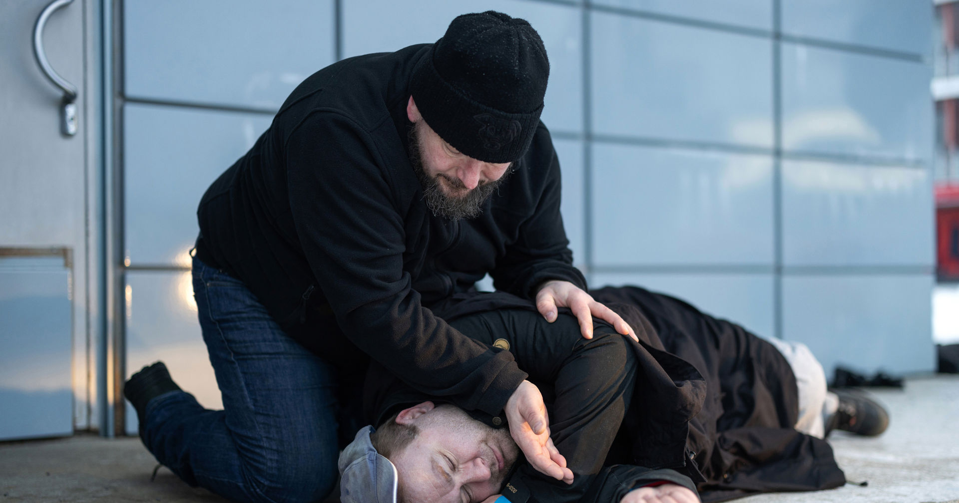 En person ligger på marken medan en annan kontrollerar om hen andas.