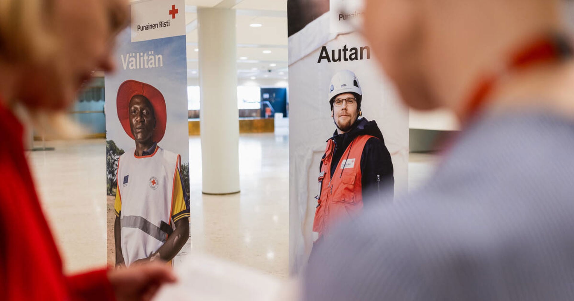 Röda Korsets roll-ups, med texten ”jag hjälper och bryr mig”, i lobbyn. Två personer läser en broschyr i förgrunden.
