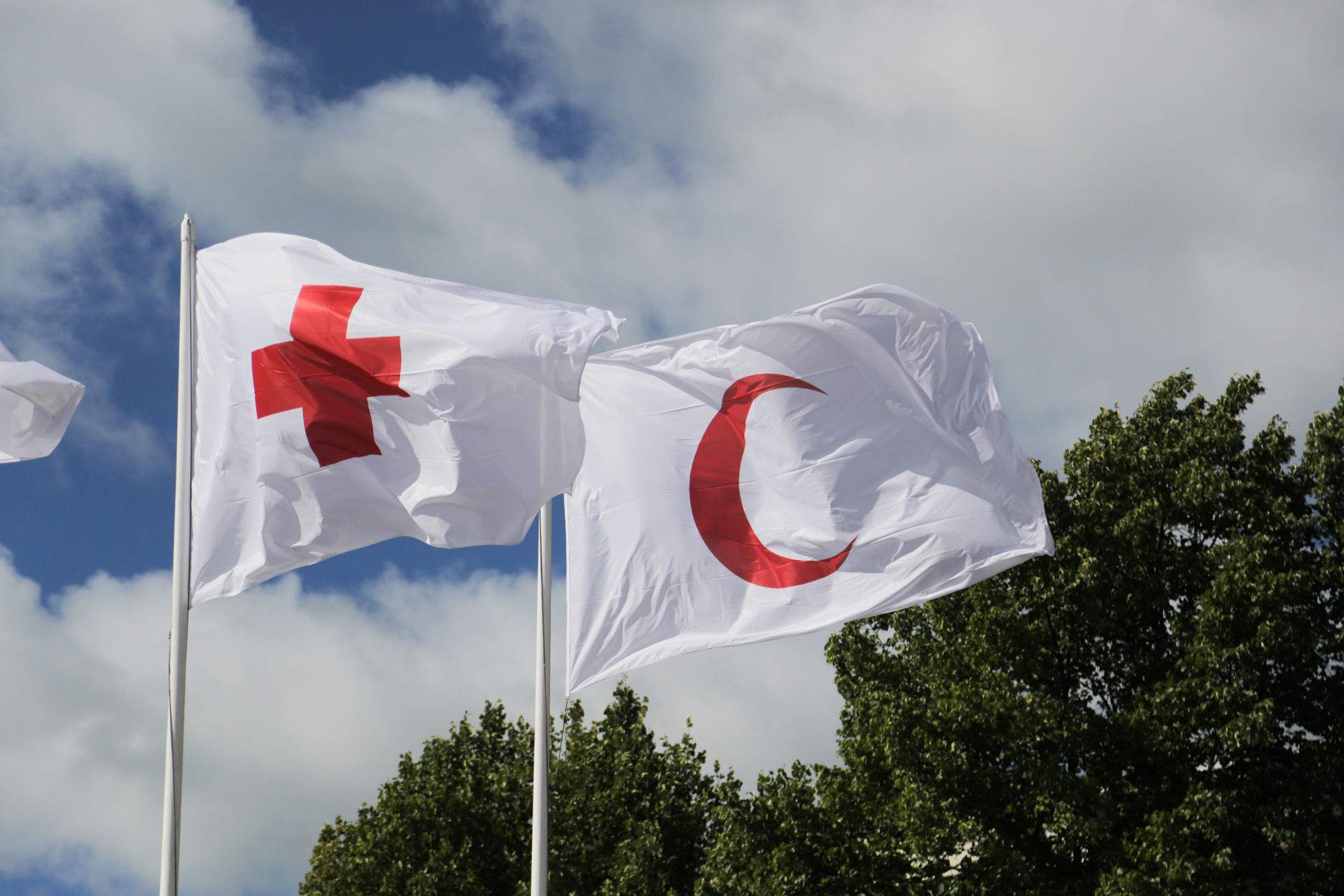 Två flaggor i flaggstängerna. Den ena har Röda Korsets symbol och den andra har Röda Halvmånens symbol.