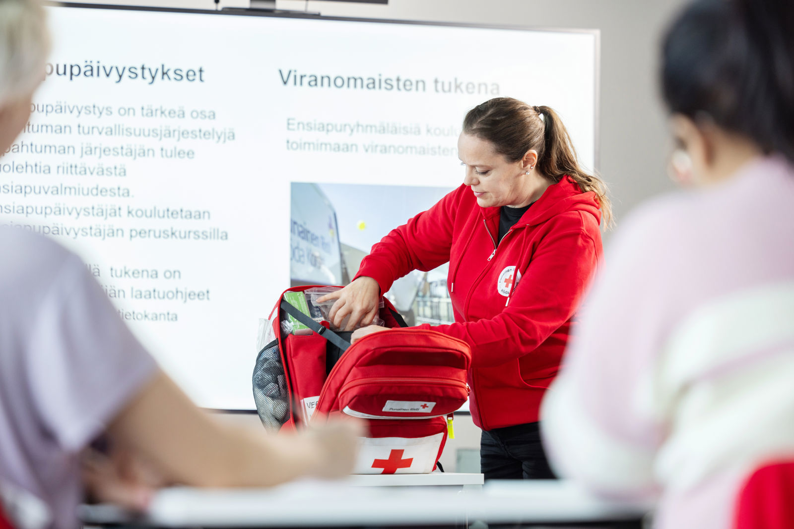 En utbildare från Finlands Röda Kors letar efter något i första hjälpen-väskan framför en vit duk.