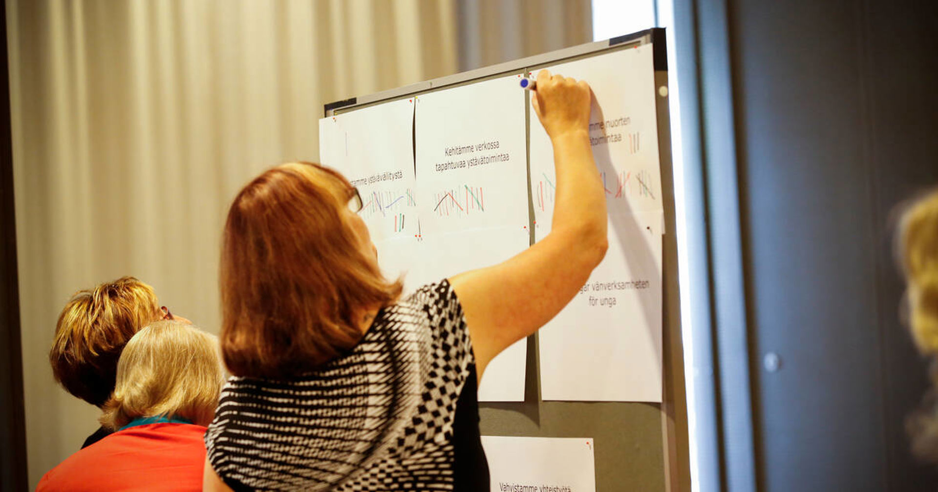 Tre personer skriver på blädderblock som sitter på väggen.