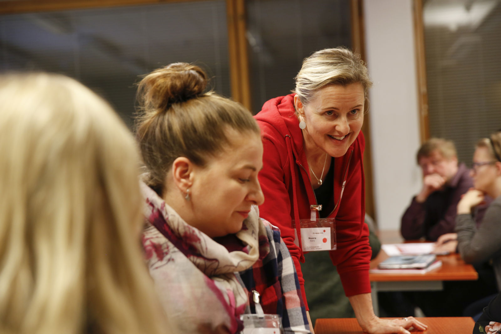 En utbildare från Finlands Röda Kors lutar sig mot bordet och ler mot deltagarna.