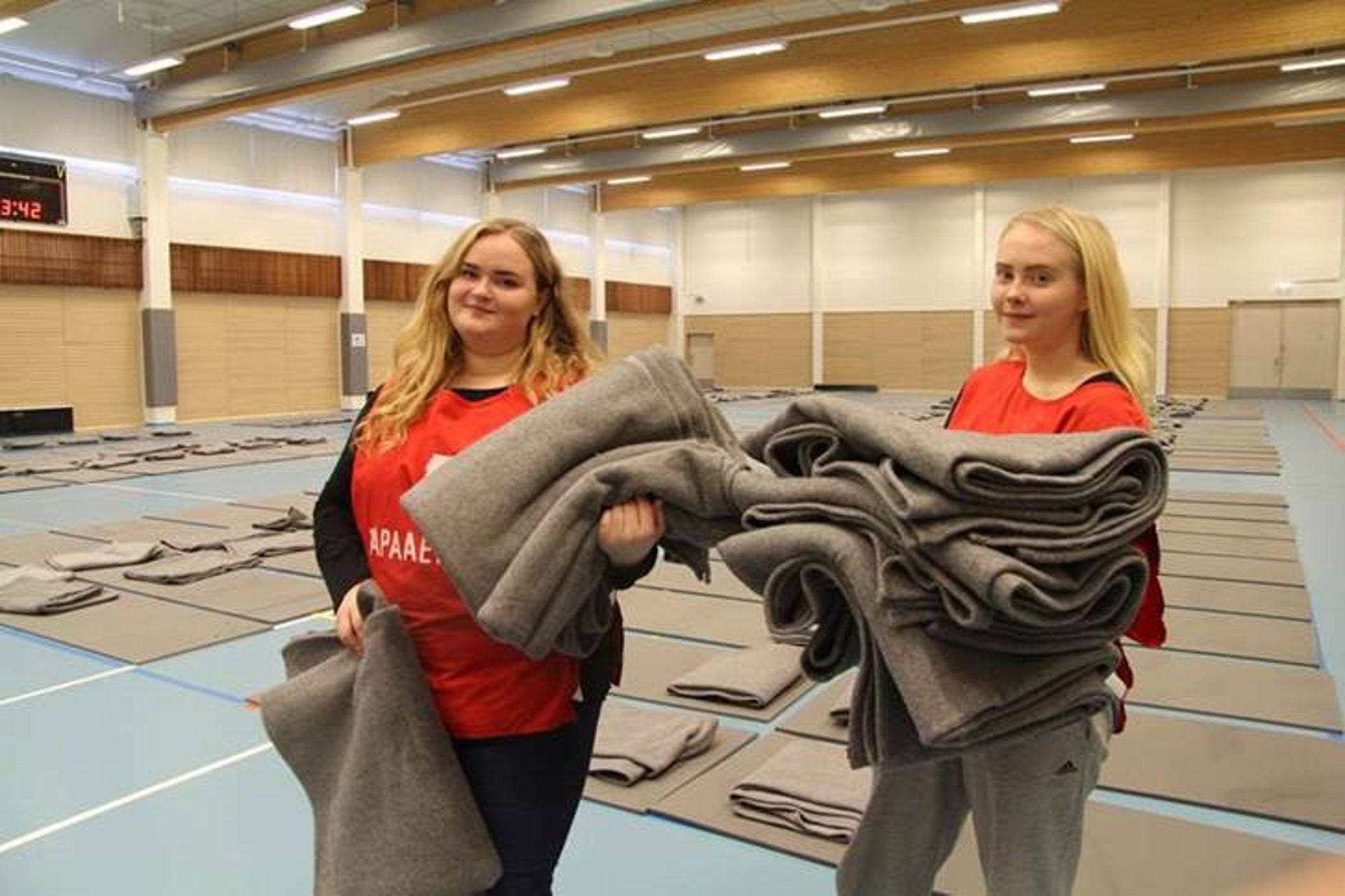 Två frivilliga från Finlands Röda Kors håller i filtar i en gymnastiksal.