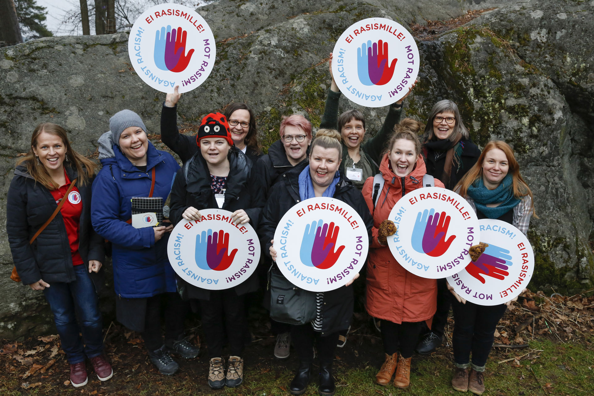 Gruppbild på utbildare i migrationsarbete utomhus. De håller logotyper för kampanjen mot rasism i händerna.