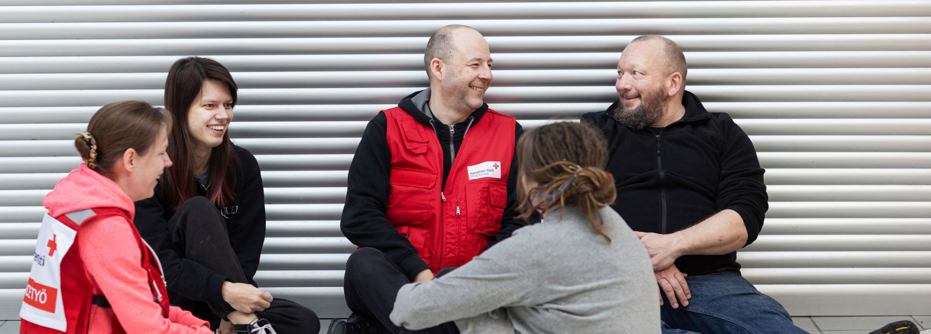 Röda Korsets frivilliga inom rusmedelsarbetet samtalar med personer på golvet. Alla ler mot varandra.