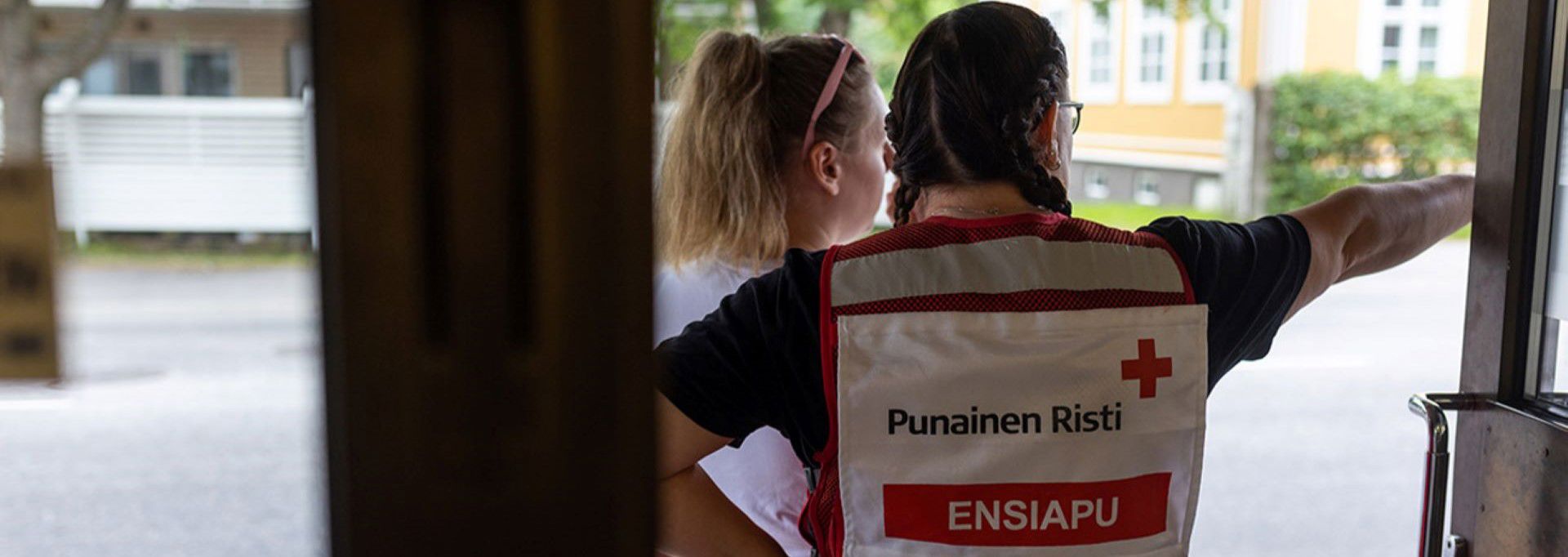 En frivillig som arbetar vid Röda Korsets första hjälpen-jour står i dörröppningen och visar vägen för en annan person. På den frivilligas väst syns texten ”Finlands Röda Kors Första hjälpen”.