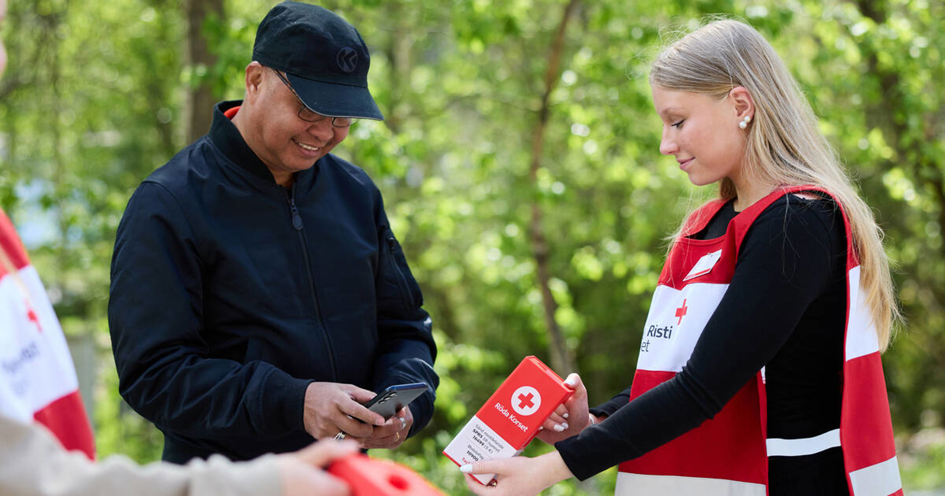 En rödakorsfrivillig räcker över en insamlingsbössa till en annan person.