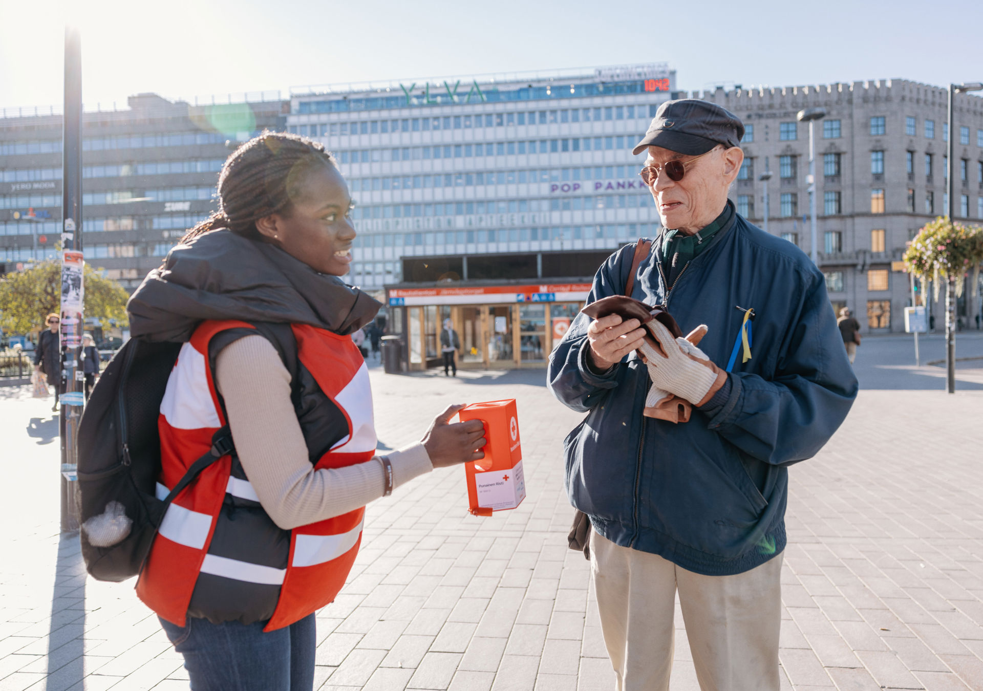 En leende person lägger pengar i Röda Korsets frivilligas insamlingsbössa.