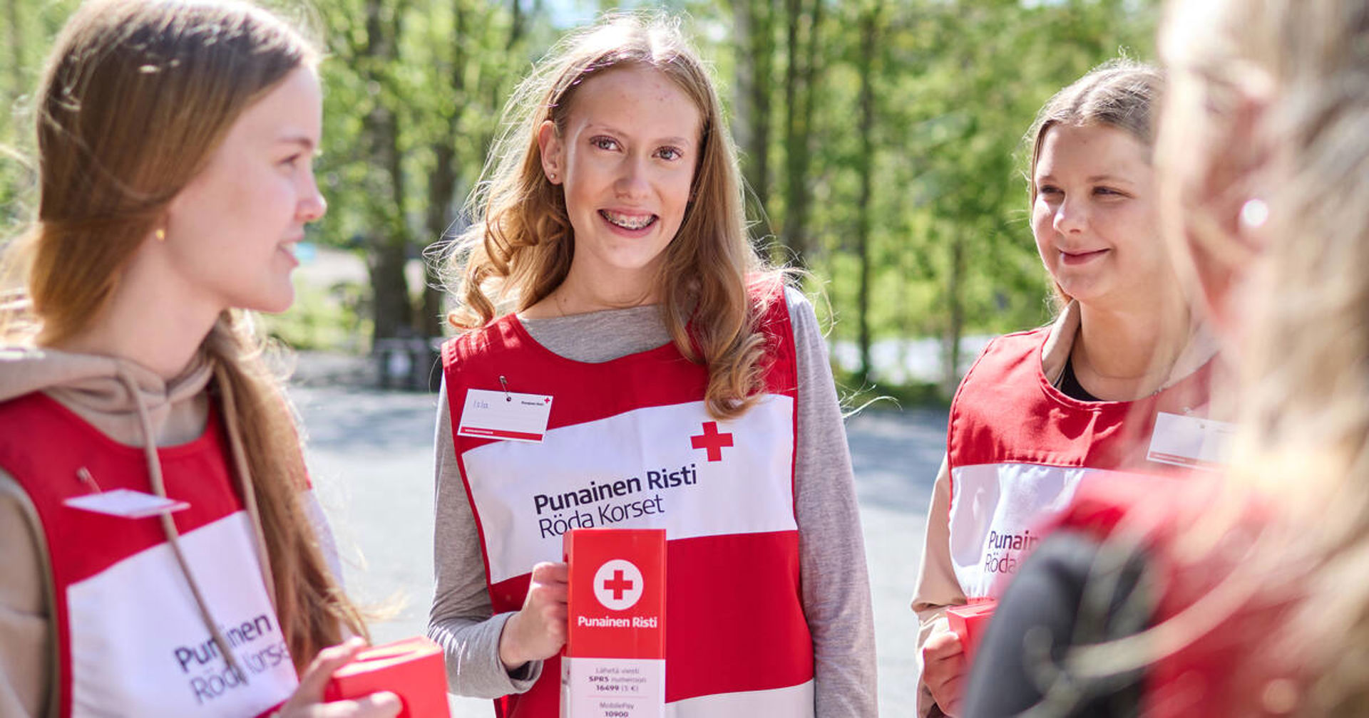 Tre skolelever lutar sig mot bänkarna med insamlingsvästar på sig och insamlingsbössor i händerna.