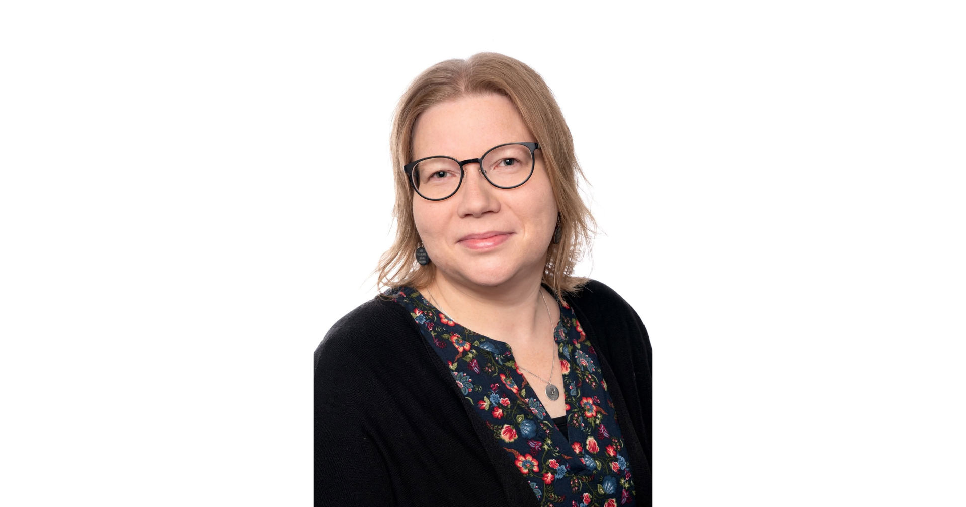 Kristiina Brisk‑Mosander tittar mot kameran, klädd i en mönstrad blus, svart kofta ja glasögon.