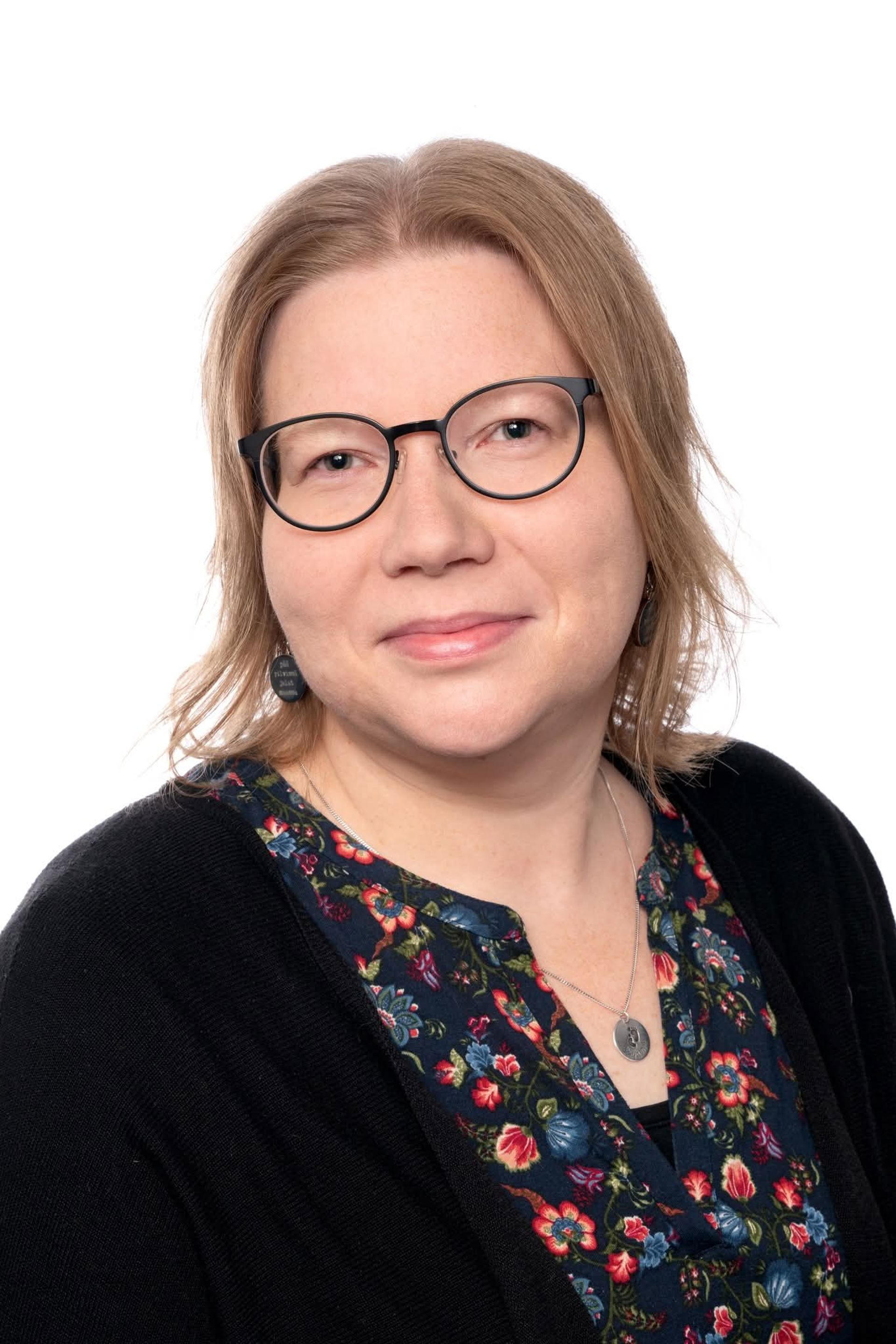 Kristiina Brisk‑Mosander tittar mot kameran, klädd i en mönstrad blus, svart kofta ja glasögon.