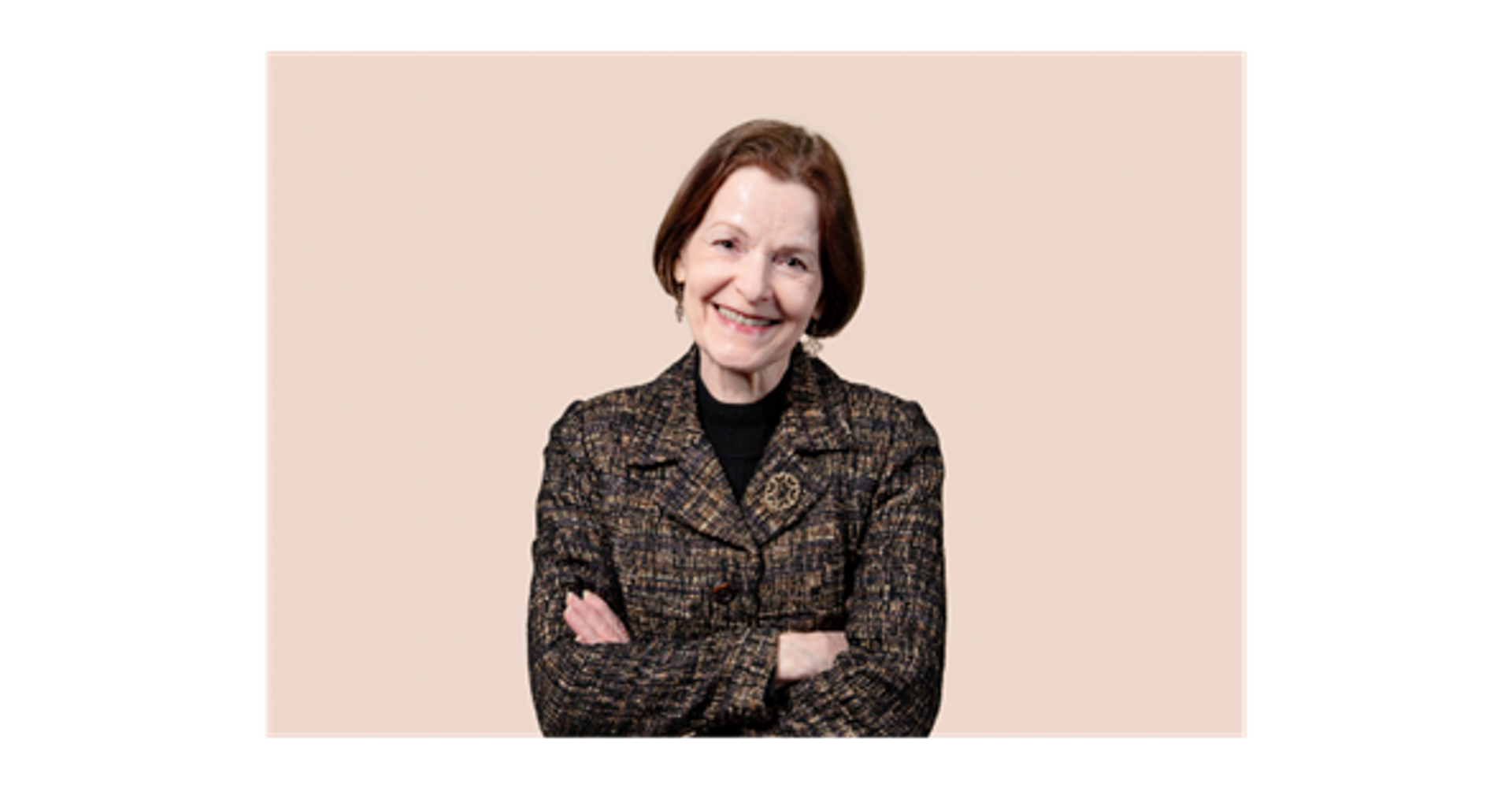 Marja Lehto står mot en ljus bakgrund med händerna i kors, klädd i en mönstrad kavaj och en mörk polotröja.