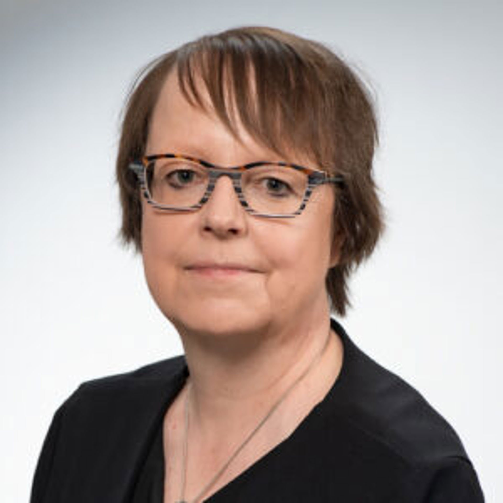 Tuula Oksanen tittar mot kameran, bärandes en svart överdel och glasögon.