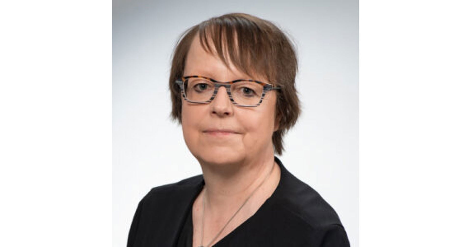 Tuula Oksanen tittar mot kameran, bärandes en svart överdel och glasögon.