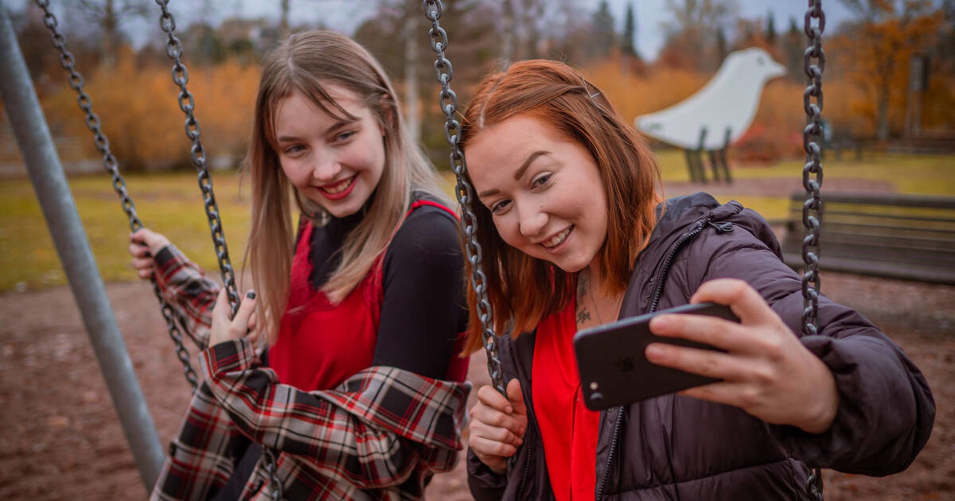 Två unga tar en bild med mobilen i gungorna.
